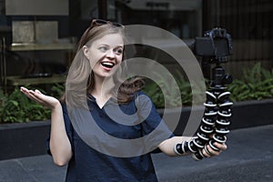 Smiling young caucasian girl woman making a video blog vlog with camera outside in the street