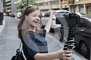 Smiling young caucasian girl woman making a video blog vlog with camera outside in the street