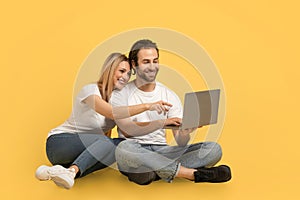 Smiling young caucasian lady hugging guy in white t-shirts show on computer, sit on floor