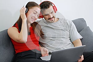 Smiling young Caucasian lover Couple listening to online music with Headphones and laptop together in living room. Lifestyle