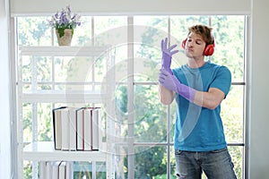 Smiling young Caucasian male Wearing violet rubber gloves for clean of housework and relaxing for listening to music with red