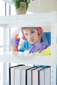 Smiling Young Caucasian male Wearing violet rubber gloves is holding Cleanser bottle and sponge. He is cleaning and wiping on