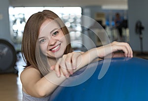 Smiling young caucasian woman girl on blue gymnastic ball at the gym, doing workout or yoga pilates exercise