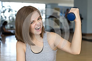 Smiling young caucasian woman girl doing workout with light dumbbells at the gym, lifting weights