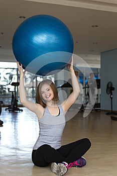Smiling young caucasian woman girl holding a blue gymnastic ball at the gym, doing workout or yoga pilates exercise