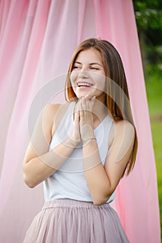 smiling young Caucasian woman with long red hair in white t-shirt relaxing in park on pink background