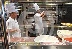 Smiling young chef in a white uniform serves traditional Italian pizza on a cruise liner MSC Meraviglia. 10 October 2018