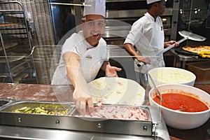 Smiling young chef in a white uniform serves traditional Italian pizza on a cruise liner MSC Meraviglia. 10 October 2018