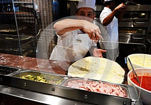 Smiling young chef in a white uniform serves traditional Italian pizza on a cruise liner MSC Meraviglia. 10 October 2018