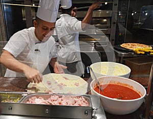 Smiling young chef in a white uniform serves traditional Italian pizza on a cruise liner MSC Meraviglia. 10 October 2018