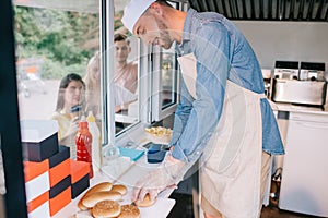 smiling young chef working in food truck while young people standing