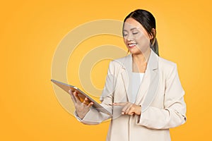 Smiling young chinese businesswoman in suit, typing on tablet, chatting