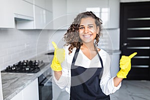 Smiling young cleaning lady with pink rubber gloves showing ok sign with thumbs up in the kitchen