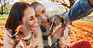 Smiling young couple with dogs outdoors in autumn park making se