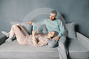 Smiling young couple embracing while looking at smartphone spending their time together at home