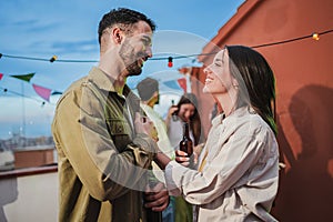 Smiling young couple flirting and having fun at a rooftop party with friends, drinking beer, enjoying and having a