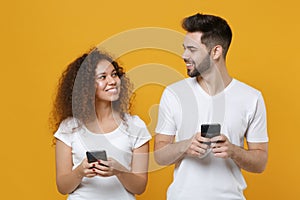 Smiling young couple friends european guy african american girl in white t-shirts isolated on yellow background. People