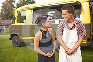 Smiling Young Couple In Front Of Food Catering Van At Summer Music Festival