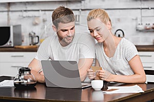 smiling young couple holding business card and using laptop together