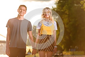 smiling young couple holding hands on river beach in evening and looking