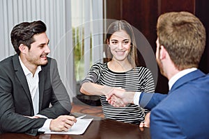 Smiling young couple shaking hands with an insurance agent