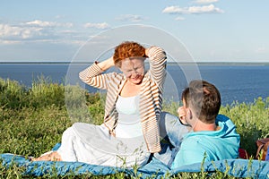 Smiling young couple sitting on grass near of water. Man laying on grass looking on happy woman