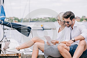 smiling young couple in sunglasses sitting and using digital tablet