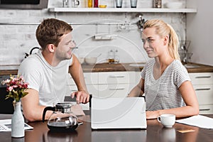 smiling young couple talking and looking at each other while using laptop together photo