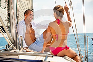 Smiling young couple talking while sitting on deck of their sailboat enjoying sea trip on sunny summer day