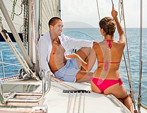 Smiling young couple talking while sitting on deck of their sailboat enjoying sea trip on sunny summer day