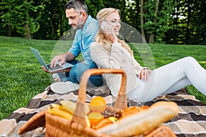 smiling young couple using smartphone and laptop at picnic