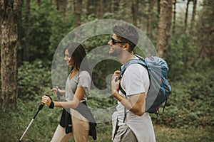 Smiling young couple walking with backpacks in the forest