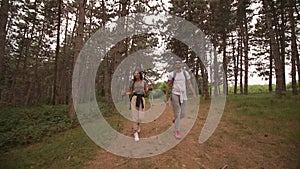 Smiling young couple walking with backpacks at the forest trail