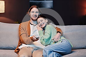 Smiling young couple watching TV at home and embracing