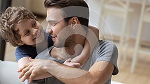 Smiling young dad and son hug relaxing at home