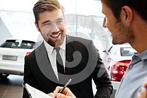 Smiling young dealer selling new car to a male customer