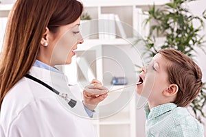Smiling young doctor examining throat to child patient