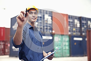 Smiling young engineer in protective work wear in a shipping yard examining cargo