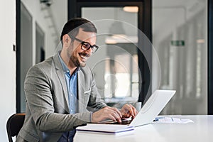 Smiling young entrepreneur typing on laptop while working at office desk