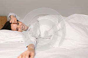 Smiling young european female sleeping on white bed, waking up, enjoying good morning, weekend