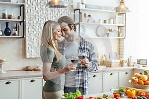 Smiling young european man with stubble and lady clinking glasses of wine, enjoy tender moment in kitchen