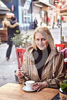 Smiling young European woman drinks coffee at street cafe in Jewish quarter of Fatih district, Istanbul