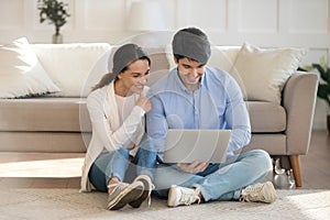 Smiling young family couple using computer together indoors.