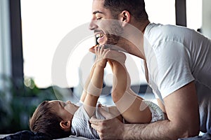 Smiling young father has fun with little baby while changing his nappy at home