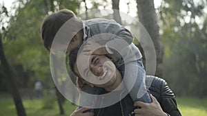 Smiling young father holding son on shoulders and playing with boy. Portrait of happy Caucasian man enjoying leisure