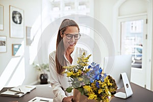 Smiling young female architect standing with flowers in her offi