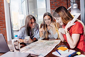 Smiling young female businesspeople looking at map sitting at work desk in modern office