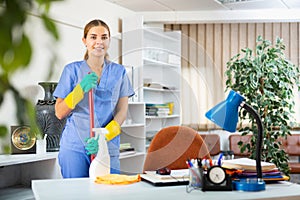 Smiling young female cleaner in uniform ready for cleaning in office