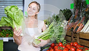 smiling young female customer holding fresh celery and leek