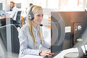 Smiling young female customer service representative with headset in call center office.